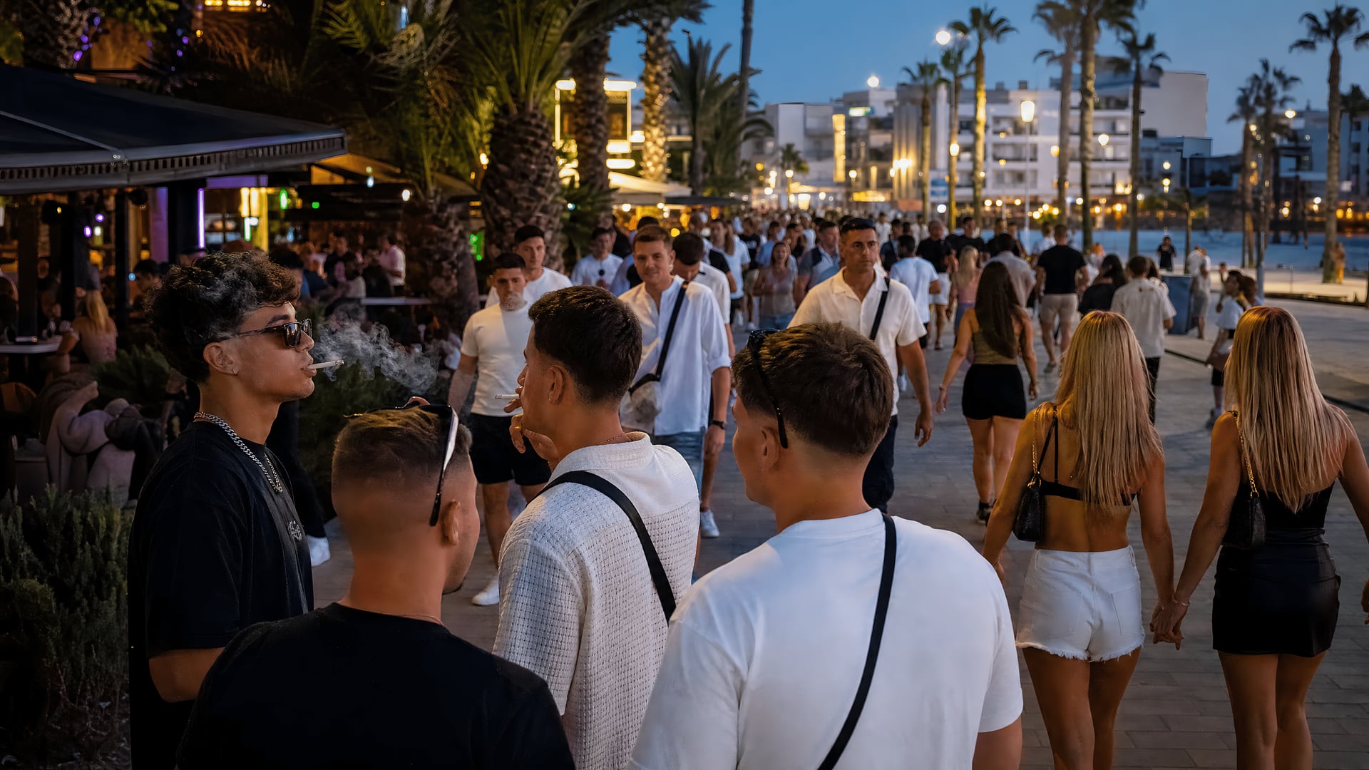 Tourists walk along a Mallorca nightlife street at dusk.
