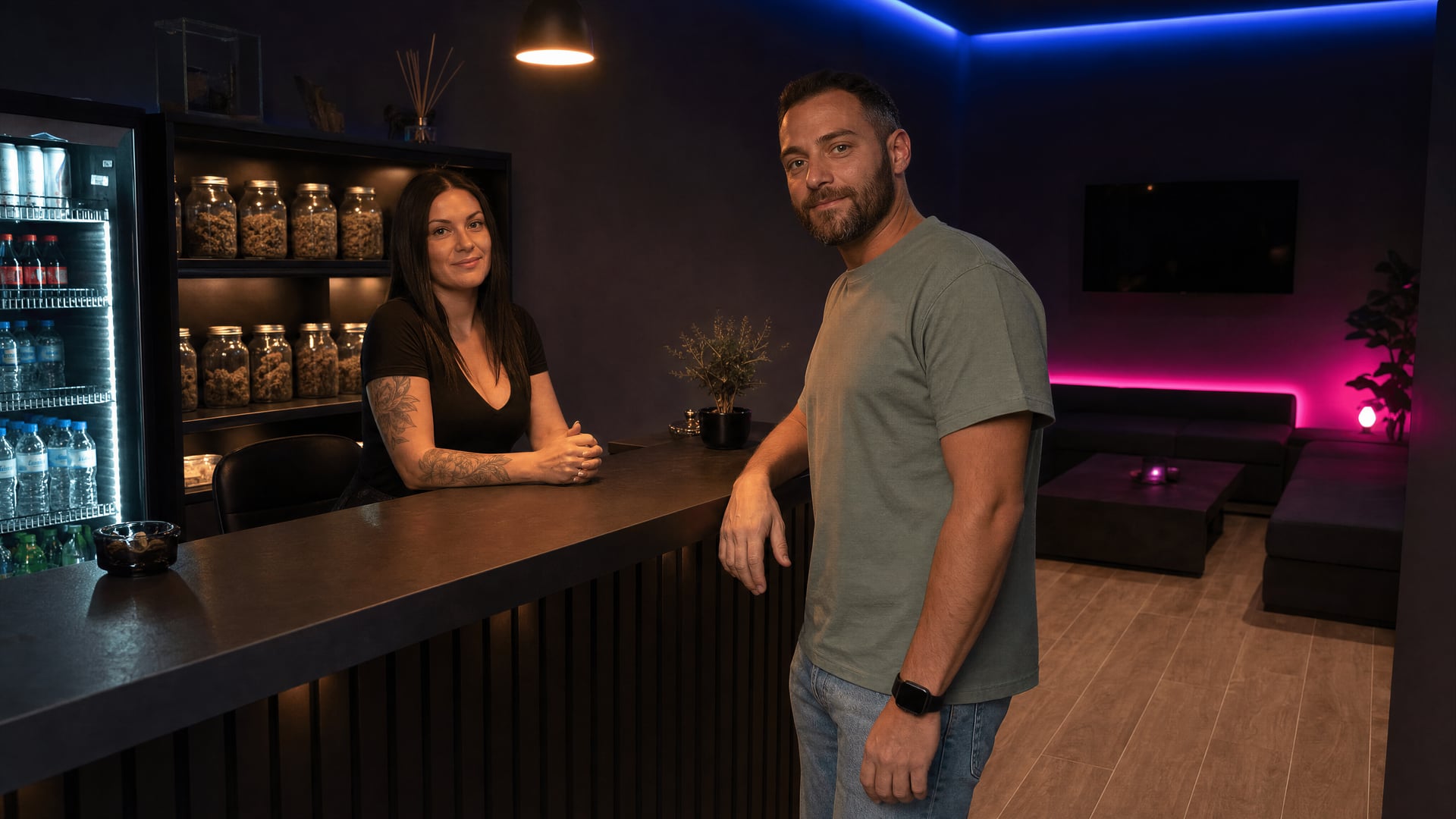 Un membre regarde l’appareil photo pendant son enregistrement auprès d’un employé au comptoir d’accueil d’une salle associative privée et sombre.